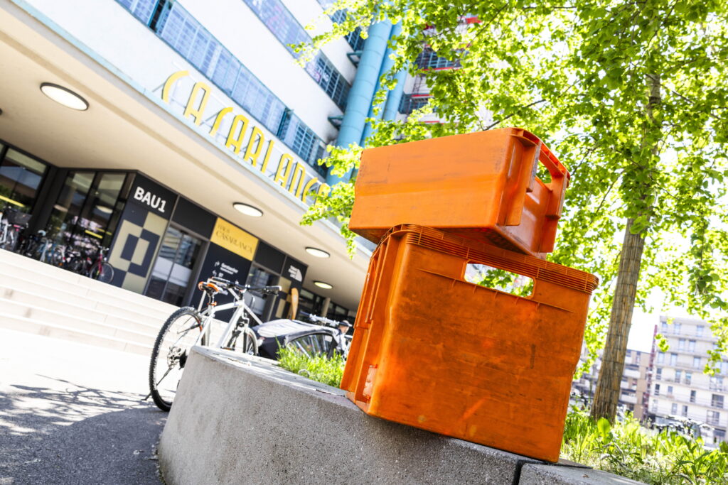 Orange Boxen stehen vor der Tabakfabrik und symbolisieren den Paketdienst