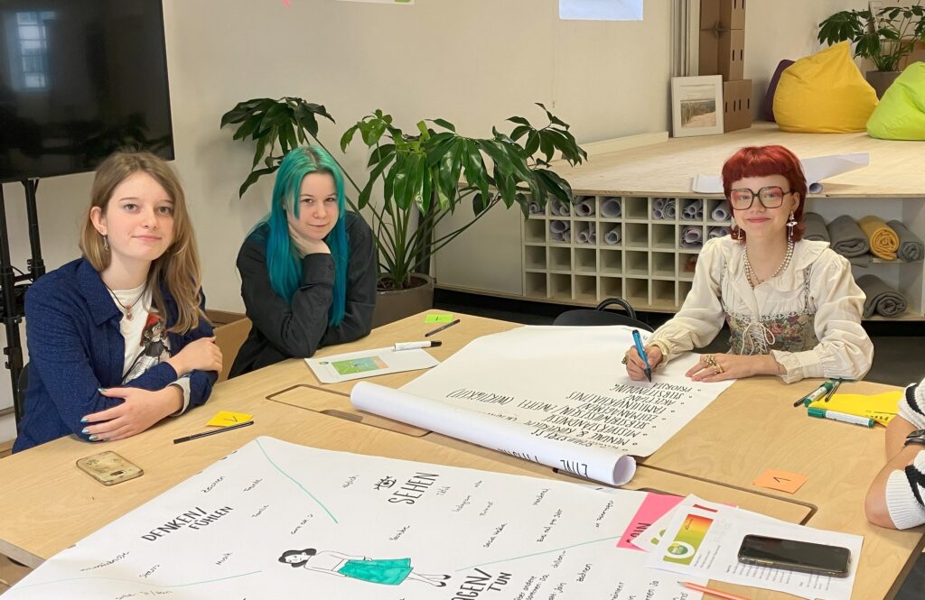 Jugendliche arbeiten an einem Tisch mit Flipchart und Buntstiften. Foto: INNERversum