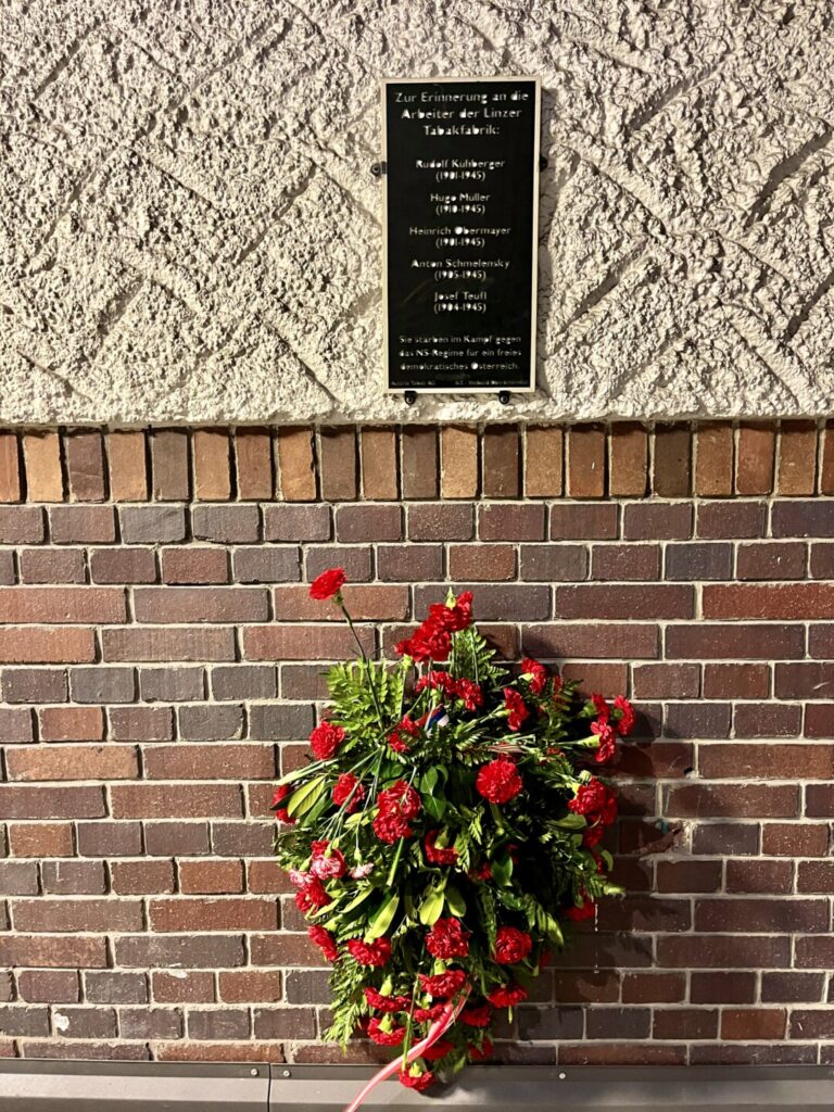 Gedenktafel zur Erinnerung an die Widerstandskämpfer der Tabakfabrik im Nationalsozialismus mit den Namen der Arbeiter Rudolf Kühberger, Hugo Müller, Heinrich Obermayr, Anton Schmelensky und Josef Teufl, mit Kranz.